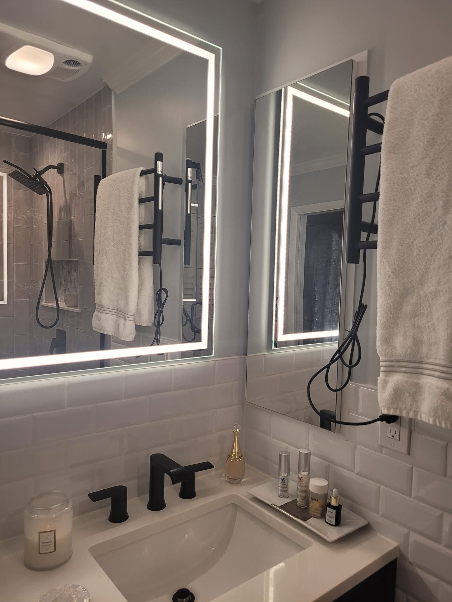 Bathroom sink with a black faucet, subway tile, and lighted mirrors